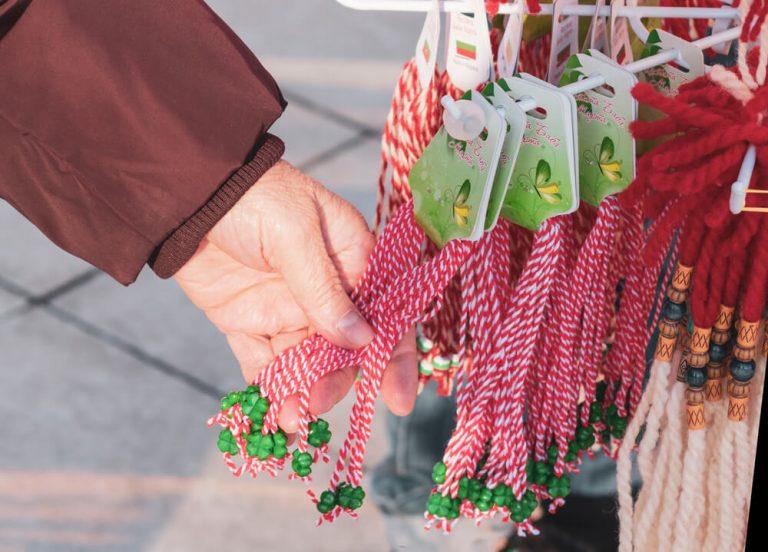 The hand of an elderly woman chooses martenitsa in a street market. Bulgarian tradition of giving jewelry from white and red threads on March 1. Selective focus